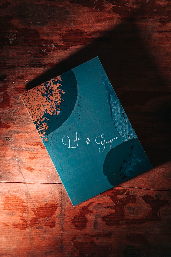 A stylish artistic wedding invitation card placed on a textured wooden surface with warm lighting.