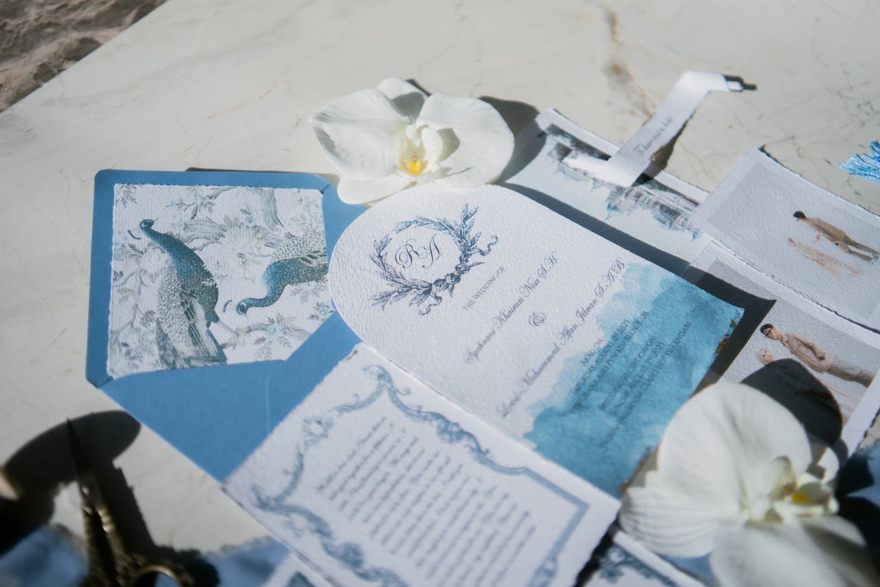 Elegant wedding invitation set featuring peacock design and white orchids on a marble background.