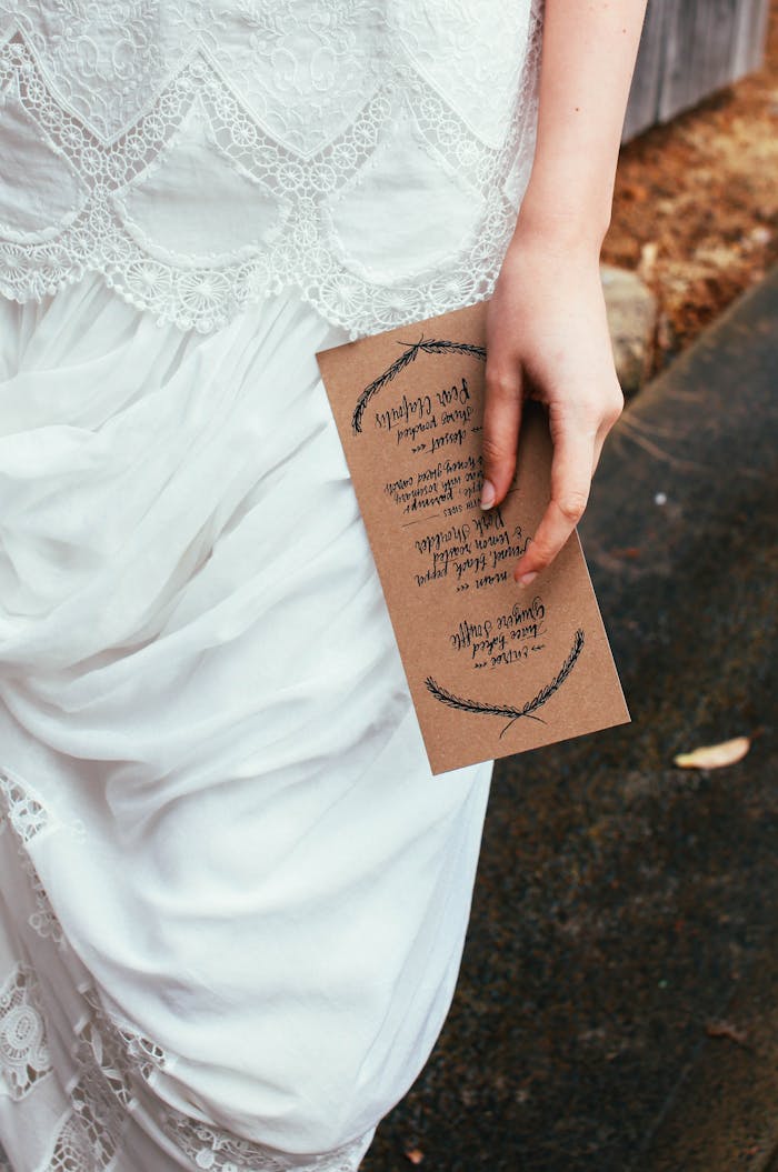 Close-up of a bride holding a wedding invitation, wearing an elegant lace gown outdoors.